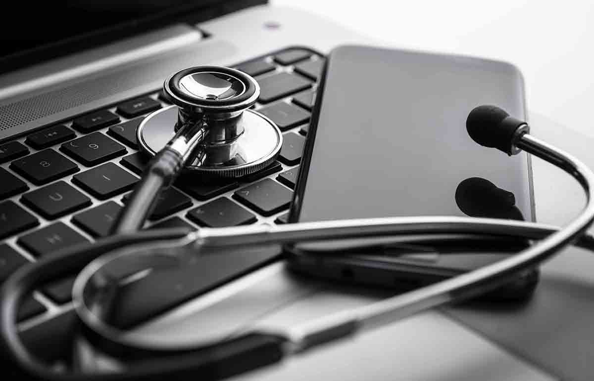 Doctor's stethoscope and cell phone resting on a laptop keyboard