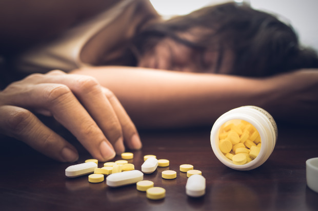 Woman taking medicine overdose and lying on the wooden floor with open pills bottle. Concept of overdose and suicide.
